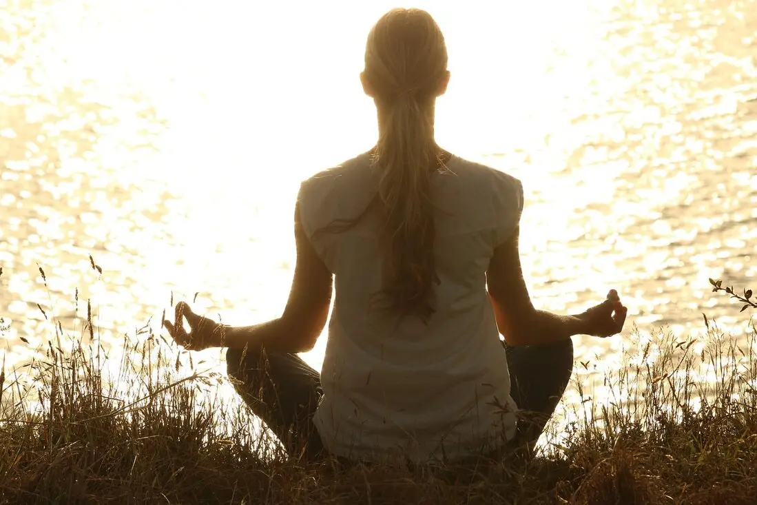 Yoga Retreat for Solo Travellers Yoga Retreat for Solo Travellers - a person sitting and meditating next to a pond with the sun reflecting of the ripples.